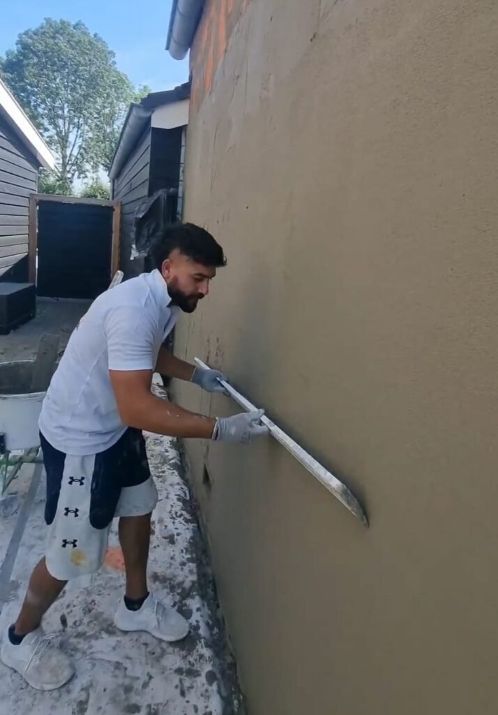 Professionele stukadoors zijn bezig met het stucen van een gevel in Krimpen aan den IJssel. Ze gebruiken gespecialiseerde gereedschappen om een gladde en gelijkmatige afwerking te creëren op de buitenmuur van het gebouw."